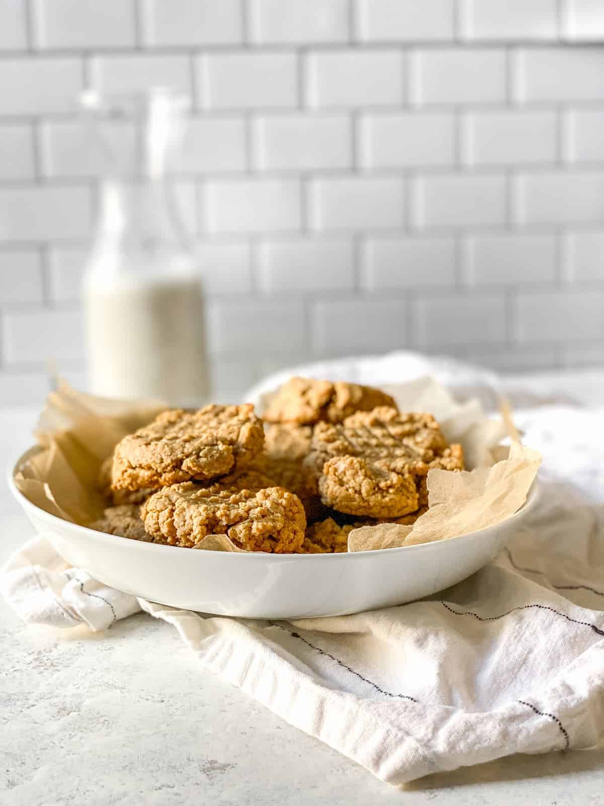 Vegan peanut butter cookies in a white bowl on a white and black striped dish towel.