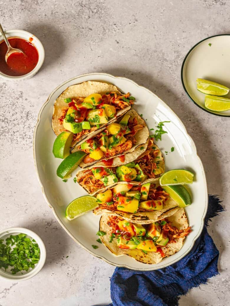 Bbq chicken tacos topped with pineapple salsa on a white platter next to a blue napkin.