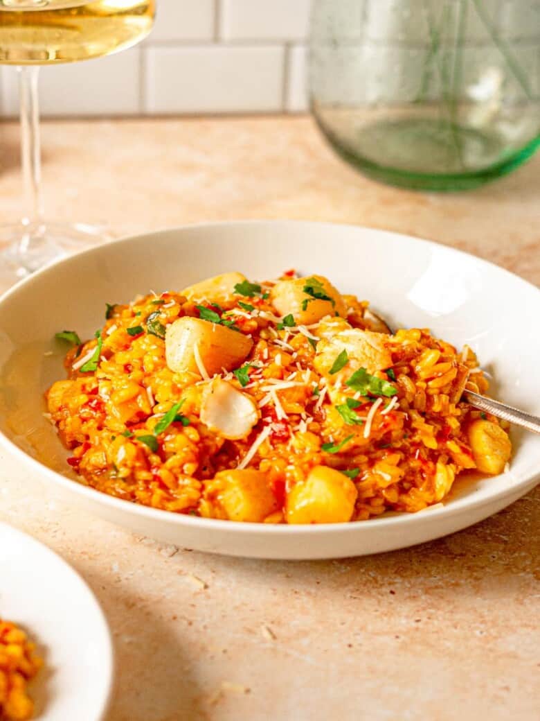 rice and seafood in a white bowl next to a glass of white wine