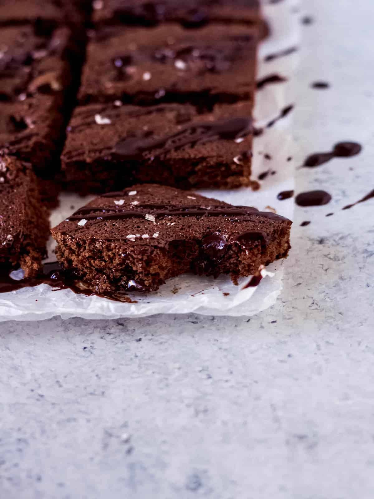 A bitten brownie piece drizzled with melted chocolate and sea salt on wax paper.