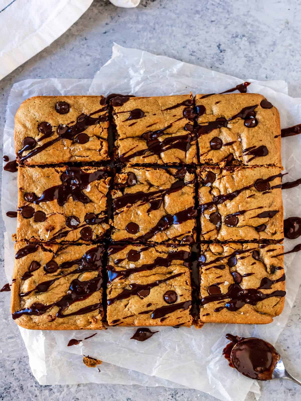 Peanut butter cookie bars drizzled with melted chocolate and sea salt on crinkly wax paper.