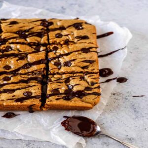 peanut butter cookie bars drizzled with melted chocolate and sea salt on crinkly wax paper