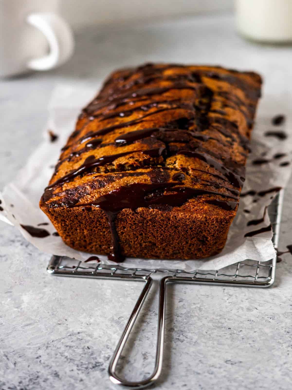 Banana bread loaf drizzled with melted chocolate on an antique cooling rack.