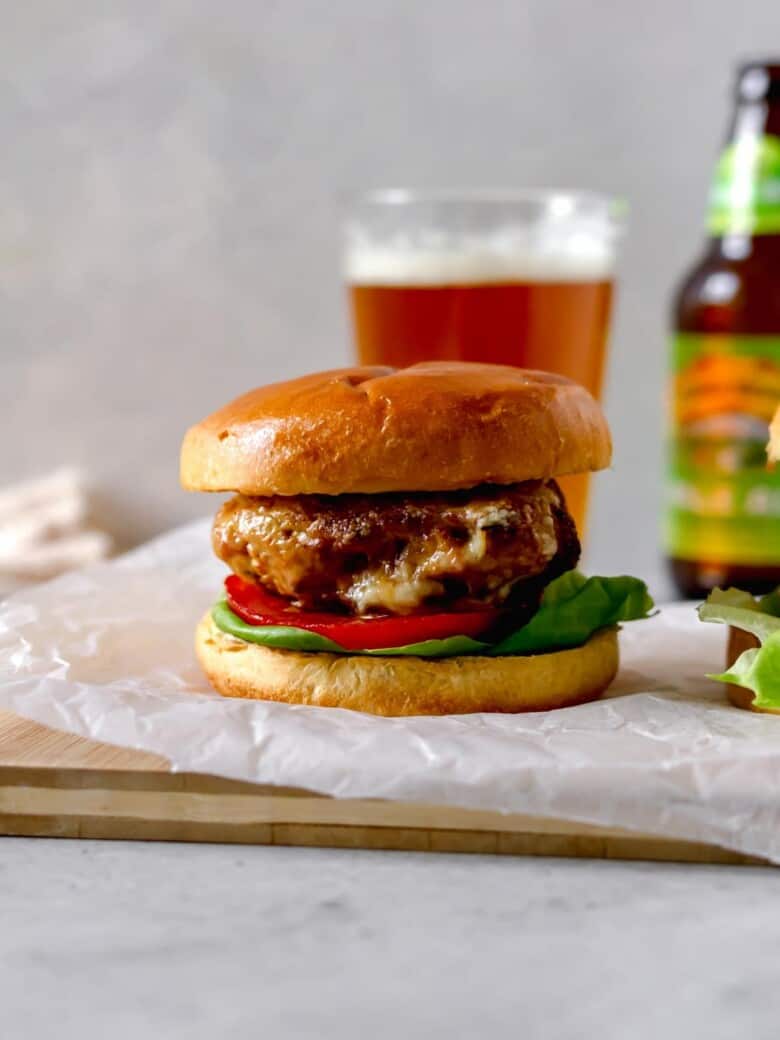 A burger on a bun with lettuce and tomato next to a glass of beer, a pickle and fries.
