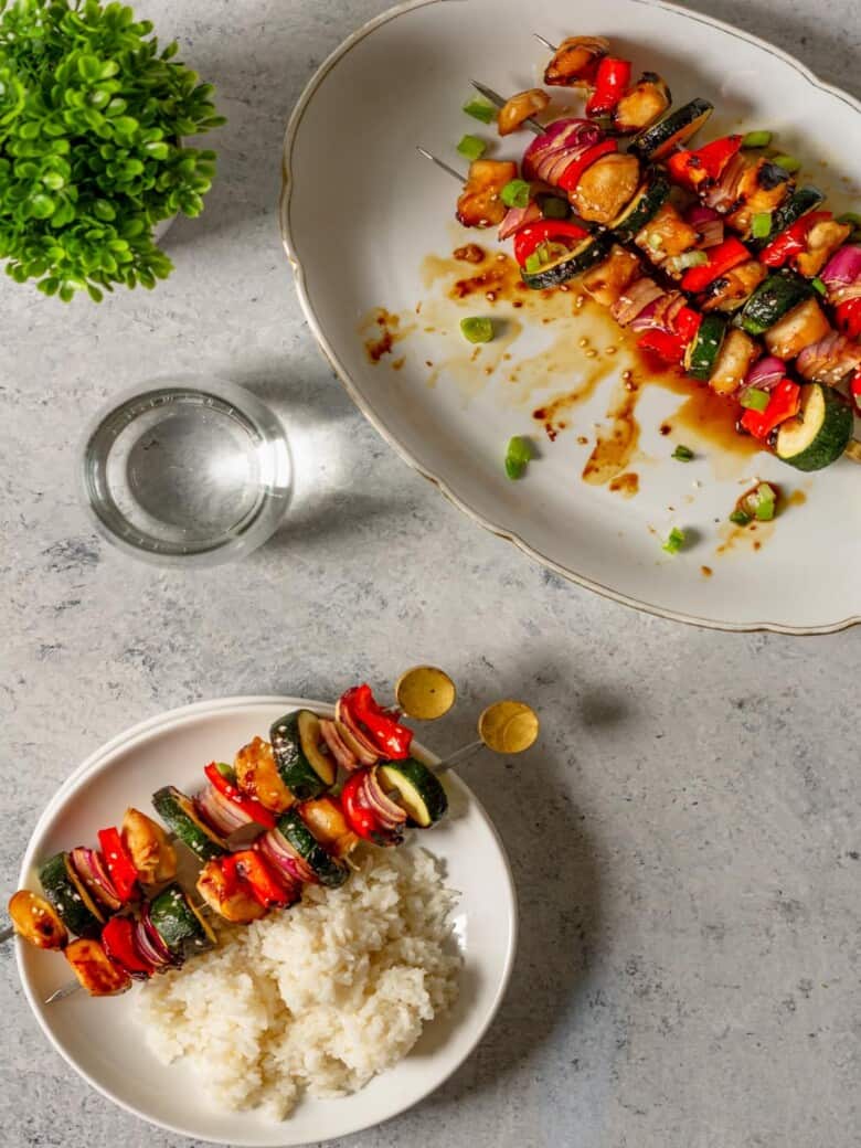 Chicken teriyaki kabobs on a serving platter next to a glass of water.