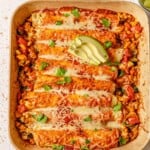 Ground turkey enchiladas topped with avocado in a brown baking dish.