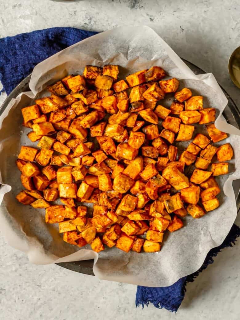 Air fryer sweet potato cubes in a basket lined with parchment paper.