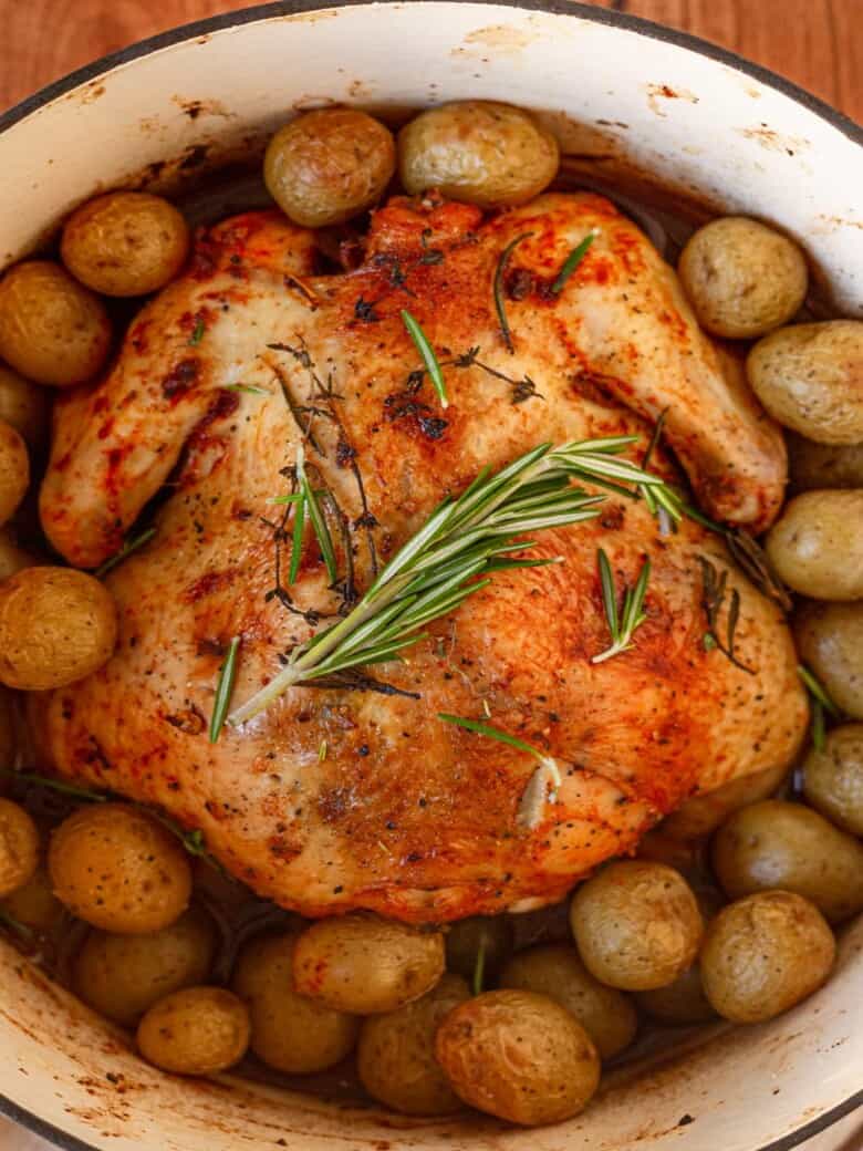 A dutch oven whole chicken and potatoes on wooden table.