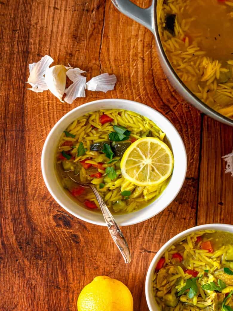 A spoon in a bowl of orzo soup next to a garlic clove.