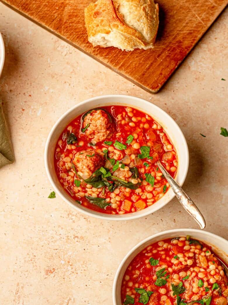 A bowl of soup next to a slice of bread.