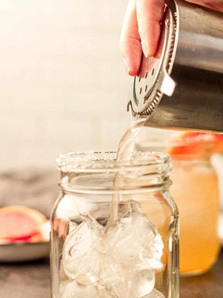 drink being poured into a glass from a cocktail shaker