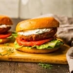 Salmon burgers with yogurt sauce on a cutting board.