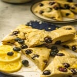 Lemon and blueberry scones stacked on a white platter with lemon slices.