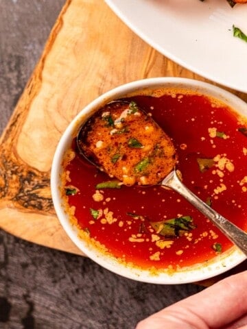 A spoon dipped into a small bowl of sauce.