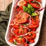 A tomato salad in a white serving dish garnished with basil.
