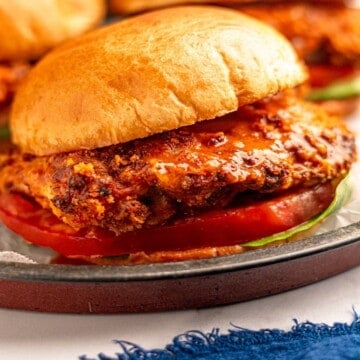 Close up view of a crispy buffalo chicken sandwich on a bun with lettuce and tomato.
