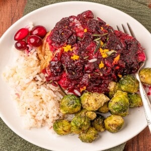 Chicken with cranberry sauce and brussels sprouts on a plate.