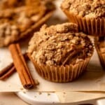 A muffin with crumb topping next to cinnamon sticks.