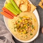 Hummus on a plate topped with dill, pickles and chickpeas.
