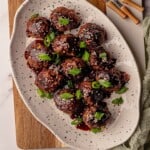 Beef meatballs topped with sesame seeds and green onions on a white plate.