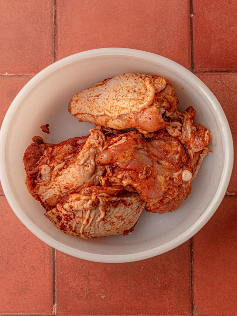 A bowl of chicken thighs with spices.