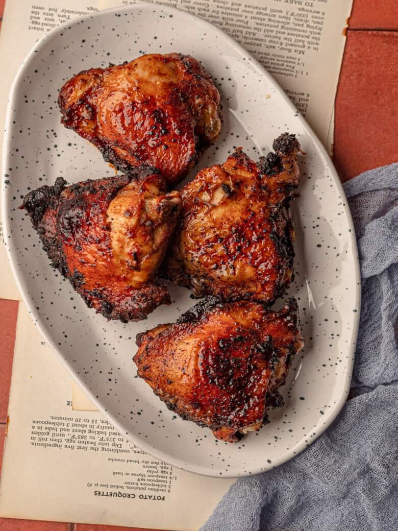 Chicken thighs on a speckled plate next to a blue napkin.