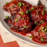 A plate of chicken thighs with bbq sauce and green onions on top.