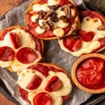Bagels with pizza toppings next to a bowl of sauce.