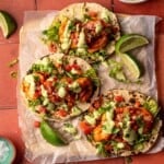 Three shrimp tacos on wax paper garnished with lime wedges.