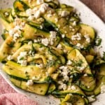 A plate of grilled zucchini slices topped with herbs and feta.