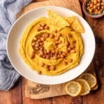 A white bowl filled with hummus that is topped with crispy chickpeas.