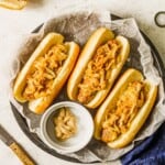 Three sausages topped with caramelized onions with a bowl of Dijon mustard.