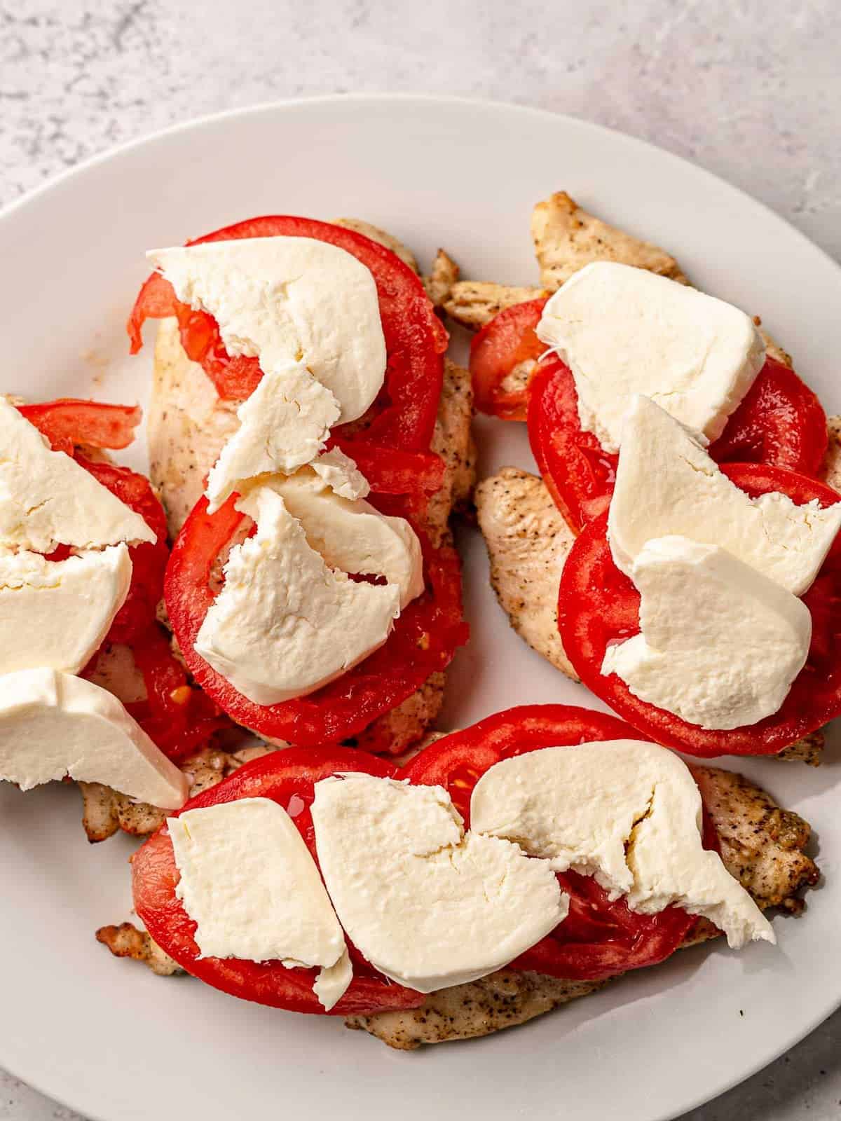 Chicken breasts topped with sliced tomato and mozzarella.