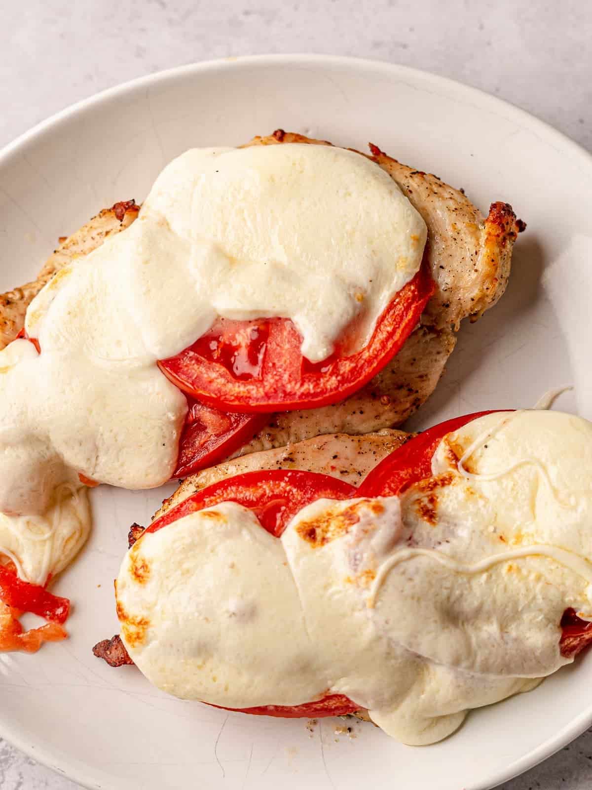 Two pieces of chicken topped with tomatoes and melted mozzarella cheese.