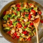 A broccoli and chicken stir fry in a pan with a wooden spoon.