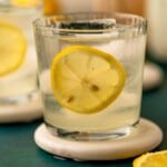 A cocktail garnished with a lemon slice on a white coaster.