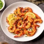 A white bowl filled with shrimp topped with lemon slices nest to a green napkin.