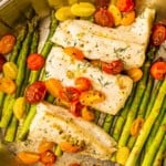 A large pan filled with asparagus, cherry tomatoes and white fish.