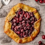Cherry galette on newspaper surrounded by fresh cherries.