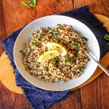 A bowl of pearl couscous topped with lemon wedges with a spoon digging in.