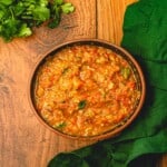 A bunch of cilantro next to a bowl filled with salsa.