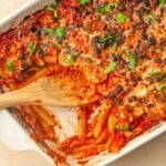 A white baking dish full of baked pasta with some scoops missing.