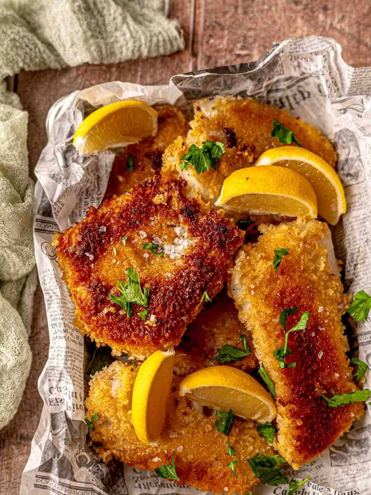 Breaded cod filets in a basket with lemon wedges.