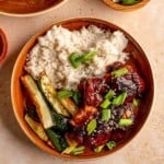 Bowl of rice, zucchini and honey chicken thighs topped with scallions.