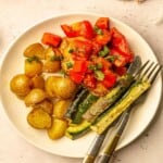 Chicken topped with tomatoes on a plate with zucchini and potatoes.