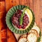 Baked brie topped with cranberry sauce in a green dish.