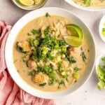 A bowl of meatball and curry soup garnished with lime wedges.