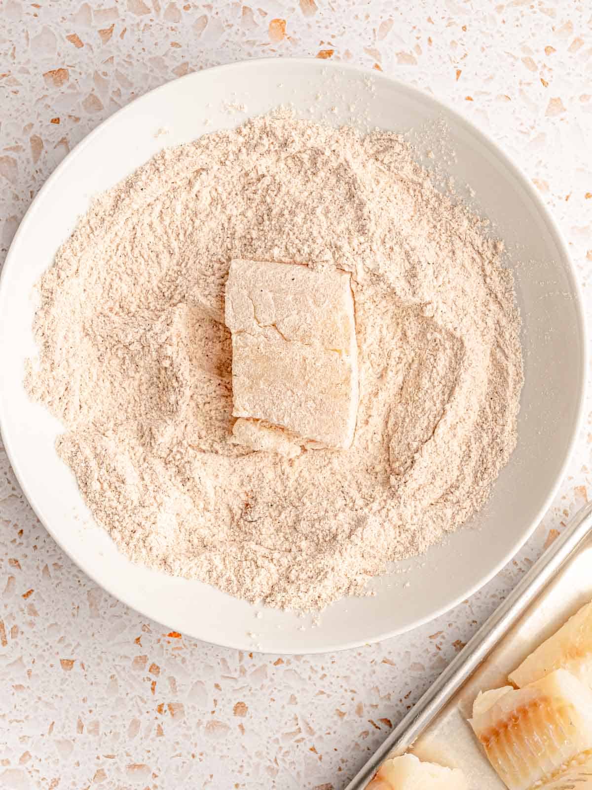 A piece of fish in a bowl of flour.