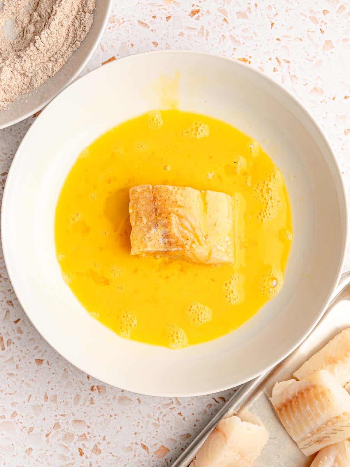 A piece of fish in a bowl of eggs.