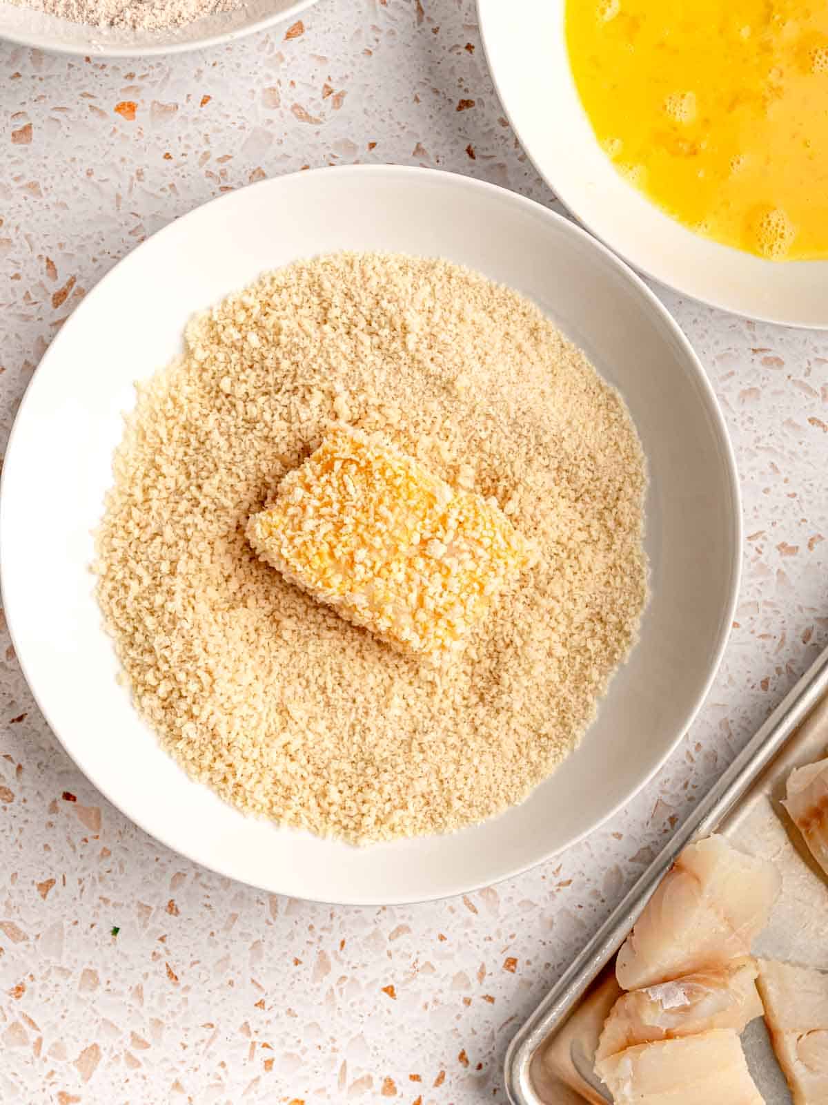 A piece of fish in a bowl of breadcrumbs.